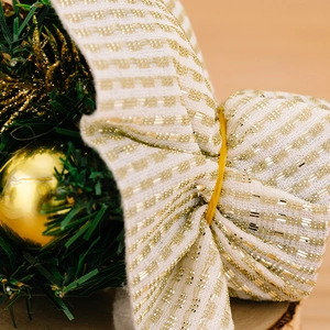 Detail of Christmas ribbon with gold stripes and miniature pine branches on wood background