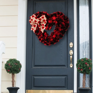 Detail of a red and black buffalo plaid heart wreath with a burlap bow on a blue door