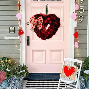 Detail of buffalo plaid heart wreath with burlap bow hanging on a pale pink wooden door