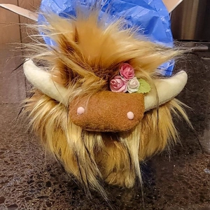 Dettaglio di un peluche di mucca Highland con pelo folto e decorazioni floreali
