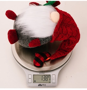 Detail view of a red knitted Valentine gnome weighing 138.7 grams on a silver digital scale