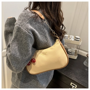 Detail of beige crossbody bag with cherry charm and brown leather chain strap