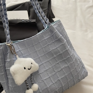 Detail of light blue pleated tote bag with woven strap and cute cloud plush charm accessory