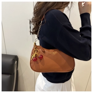 Détail du sac bandoulière en cuir marron avec breloque cerise et chaîne dorée