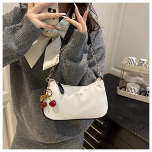 Detail of white leather shoulder bag with red cherry pendant and black strap accents