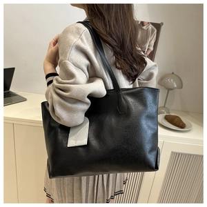 Close-up of large black leather tote bag with a grey charm and textured finish