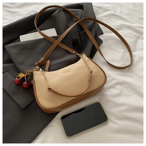 Detail of a beige moon-shaped bag with brown strap, gold chain, and cherry charm