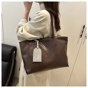 Detail of dark brown tote bag with matte texture and decorative cream hangtag