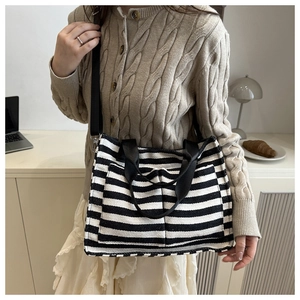 Detail of striped canvas tote bag showing the front pocket and adjustable shoulder strap