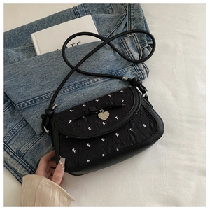 Close-up of bow decor and silver heart charm on black printed crossbody saddle bag