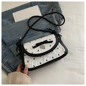 Detail of quilted white crossbody bag with black bow and heart-shaped metal pendant