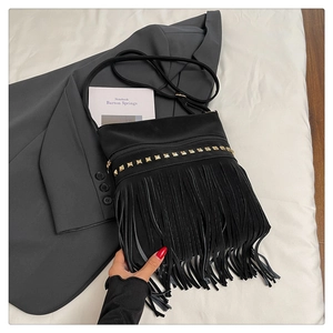 Détail d'un sac bandoulière noir à franges et clous dorés sur un fond de style épuré