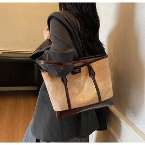 Detail of a beige suede tote bag with brown leather accents on a model's shoulder