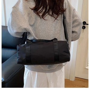 Vista posteriore della modella con borsa cilindrica nera in nylon e tracolla