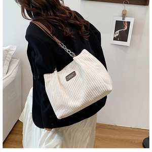 Detail of white corduroy tote bag featuring brown leather strap and metal chain