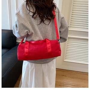 Red cylindrical waterproof nylon gym bag with adjustable shoulder strap worn by a model