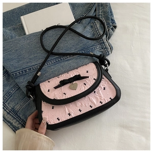 Close-up of pink textured fabric with black bow and heart pendant on crossbody bag