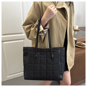 Quilted black nylon tote bag shown on a shoulder in a cozy interior cafe setting