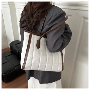 Detail view of white quilted tote bag with brown straps worn over a grey blazer