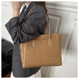 Close-up of a khaki quilted tote bag worn over the shoulder showing large capacity