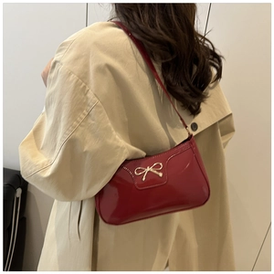 Red patent leather baguette bag with gold bow clasp styled on shoulder for casual look