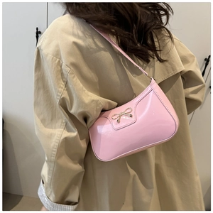 Pink patent leather underarm bag with golden bow clasp shown on a beige trench coat