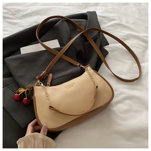 Detail of beige litchi grain bag with gold chain strap and red cherry charm decoration