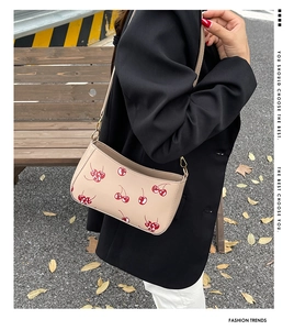 Detail of beige shoulder bag with red cherry print worn by model in street scene