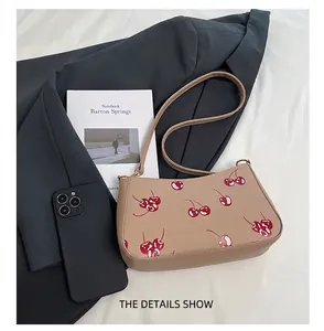 Detail view of cherry print baguette bag next to a smartphone for size comparison