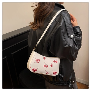 Detail of white PU shoulder bag with red cherry prints worn by a model in black leather jacket