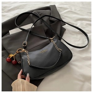 Detail of black lychee grain leather bag with gold logo and cherry charm accessory