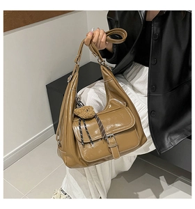 Detail of a brown patent leather hobo bag with teddy bear charm on female model