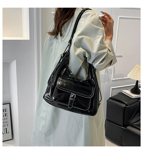 Detail of black glossy hobo bag featuring white contrast stitching and a buckle flap pocket