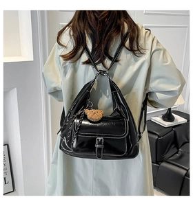 Black patent leather backpack with contrast stitching and bear charm shown on model