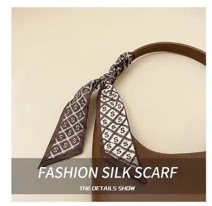 Detail of a silk scarf with 'S' print tied in a bow on a brown leather handbag