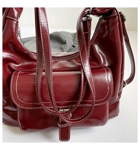 Close-up of wine red glossy leather shoulder bag with bold white contrast stitching