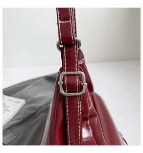 Macro detail of wine red patent leather shoulder bag with white contrast stitching and silver buckle