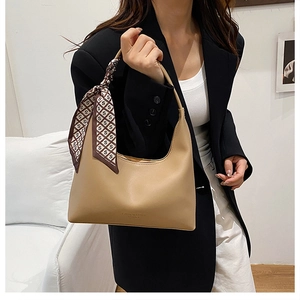 Close-up of khaki underarm bag with decorative silk scarf handle and leather detail
