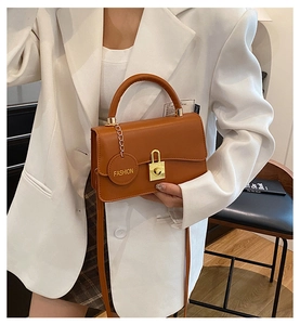 Dettaglio della borsa a spalla in pelle marrone con chiusura dorata e ciondolo moda