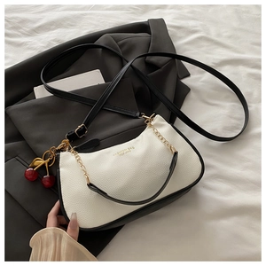 Detail of white litchi pattern leather bag with black trim and cherry pendant