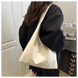 Detail of a large cream-colored hobo shoulder bag worn by a model in a minimalist indoor setting