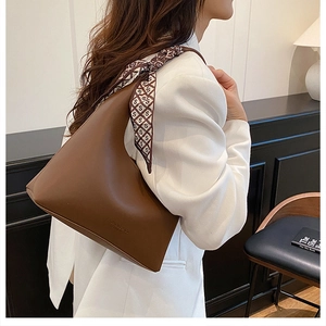Detail of a brown leather hobo bag with an elegant silk scarf wrapped around the handle