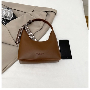Detail of a brown crescent handbag with a geometric silk scarf and embossed text logo
