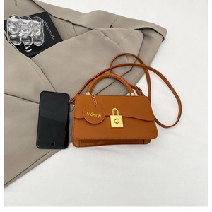 Dettaglio borsa in pelle caramello con chiusura dorata e ciondolo con scritta