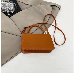 Borsa a mano a trapezio marrone caramello con dettagli dorati su blazer grigio