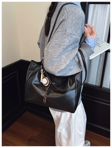 Detail of black leather tote bag featuring a sporty baseball charm and delicate logo patch