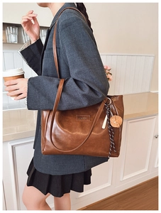 Brown vintage tote bag detail with fashion metal label and hedgehog pendant on a shoulder strap