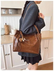 Detail of deep brown tote bag with fashion tag and decorative bag pendant accessory