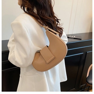 Model wearing a camel crescent shoulder bag with a wide strap and matte leather finish