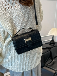 Fashionable black quilted crossbody bag with gold buckle on a model in white sweater
